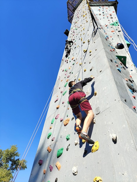 ティーンエイジャーの少年が特別な塔の登山壁に登って訓練をしています