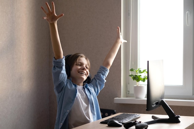 A teenage boy is sitting at home at a computer and playing computer games. Rejoices in victory.