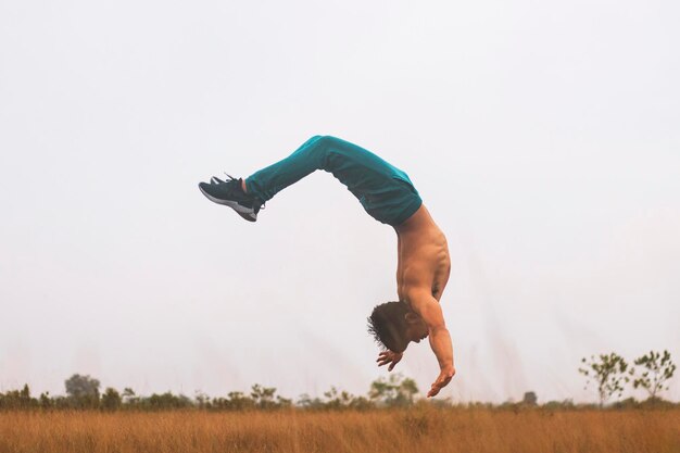 Teenage boy jumping upside down on land against clear sky