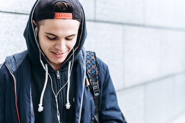 Teenage Boy Listening To Music And Using Phone In Urban Setting