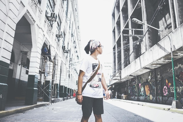 Foto ragazzo adolescente che guarda da un'altra parte mentre si trova sulla strada tra gli edifici della città