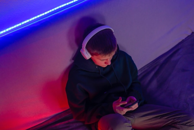 Photo teenage boy playing on phone in his room with neon light