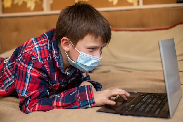 Teenage boy in protective medical mask coughs in fist.  Distant remote self education.
