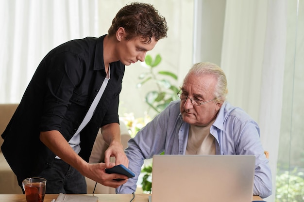 teenage boy showing grandfather how to pay bills via mobile application