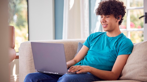 Photo teenage boy sitting on sofa at home using laptop computer