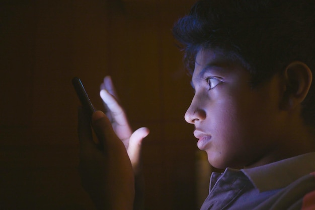 Teenage boy sitting on sofa using smart phone at night