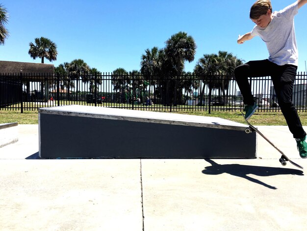 写真 晴れた日に青い空を背景にスケートボードをしている10代の少年