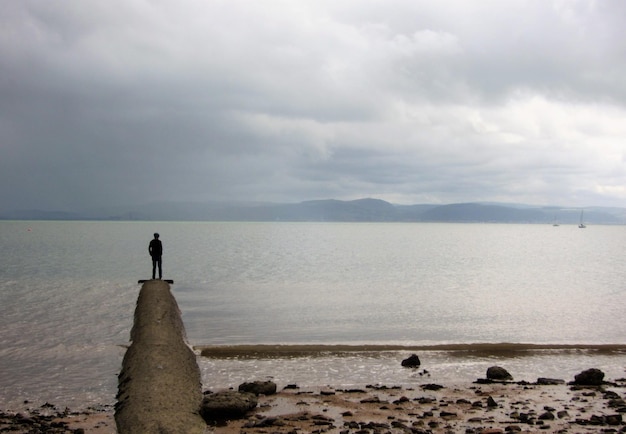 Teenage boy standing on jetty against sea during sunset