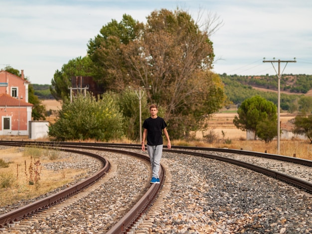 teenage boy standing on railroad track against sky