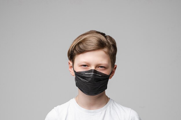 Teenage boy stands in black medical mask, portrait isolated