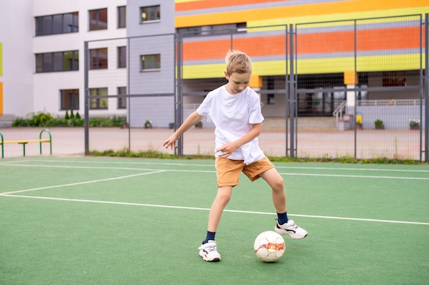Un adolescente si trova su un campo verde nel cortile della scuola con un pallone da calcio in allenamento