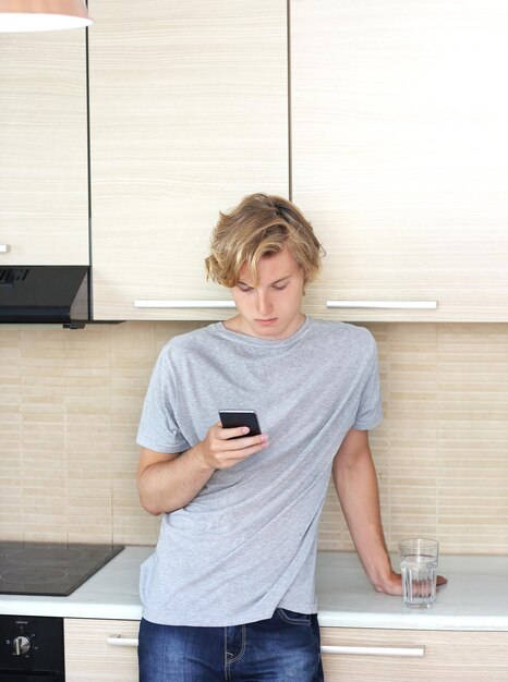 Teenage boy typing text messageStanding in the kitchenUsing smart phone