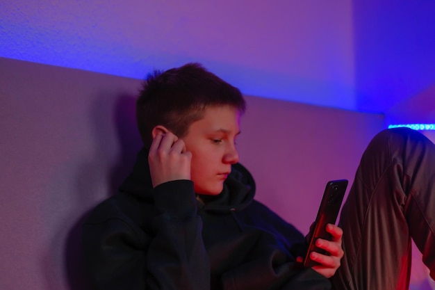 Teenage boy using phone and headphone in his room with neon light