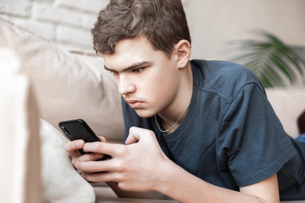 家のソファに横たわってスマートフォンを使っているティーンエイジャーの少年