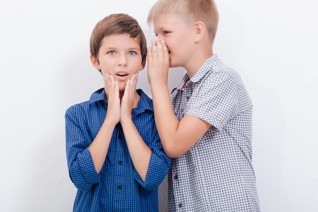 Teenage boy whispering in the ear a secret to friendl on white background