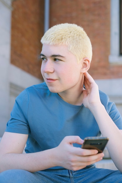 teenage boy with yellow hair and cell phone in hand outdoors