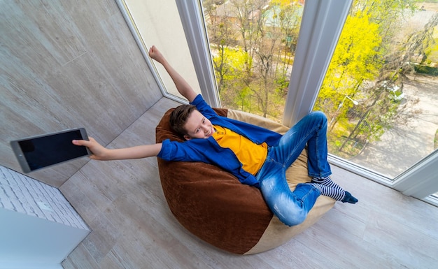 L'adolescente ha vinto il videogioco kid che si rilassa sul balcone con alberi verdi all'esterno
