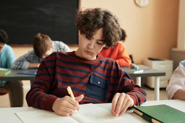 Teenage boy writing in notebook during school class