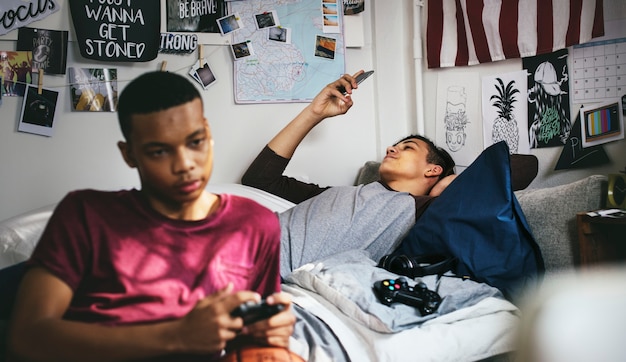 Teenage boys hanging out in a bedroom playing a video game and using a smartphone