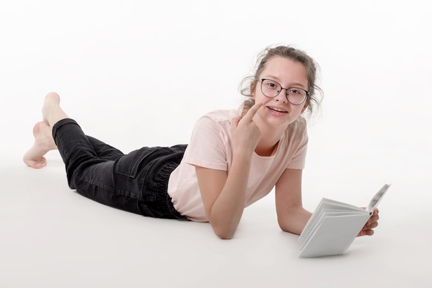 Teenage caucasian girl with glasses is lying and reading book on white background