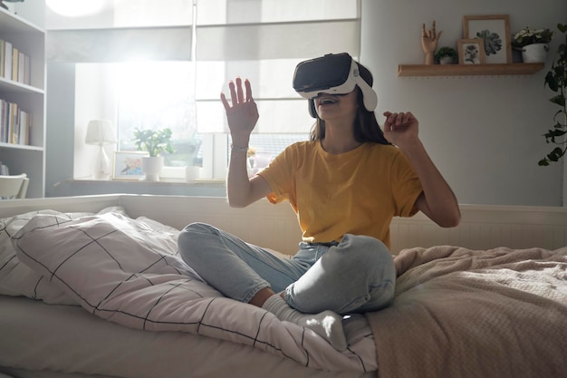 Teenage caucasian woman using Virtual reality glasses while sitting in bedroom