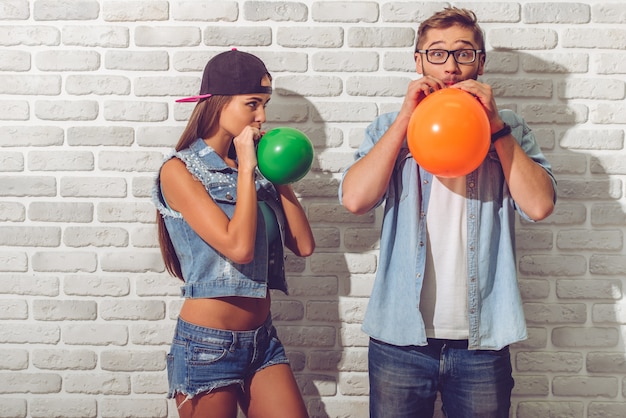 Подростковая пара в джинсовой одежде и кепках дует воздушные шары