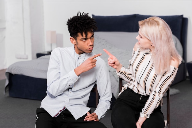 Teenage couple sitting on chair arguing and pointing finger on each other