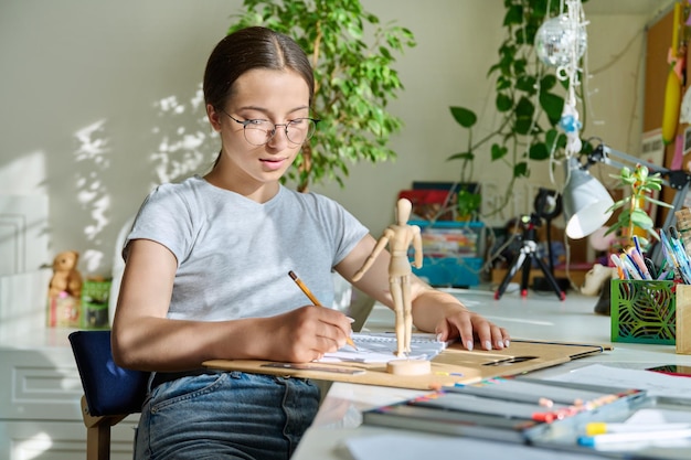 Teenage creative girl artist drawing with a pencil sitting at the table at home