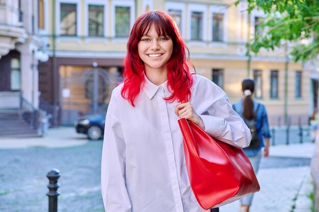 Teenage fashionable smiling female with red dyed hair looking at camera urban style street background copy space Youth fashion beauty trends people concept