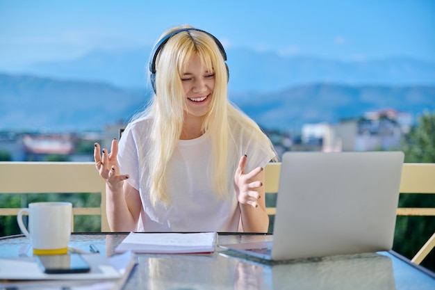 Teenage female student in headphones studying online using laptop for video conference