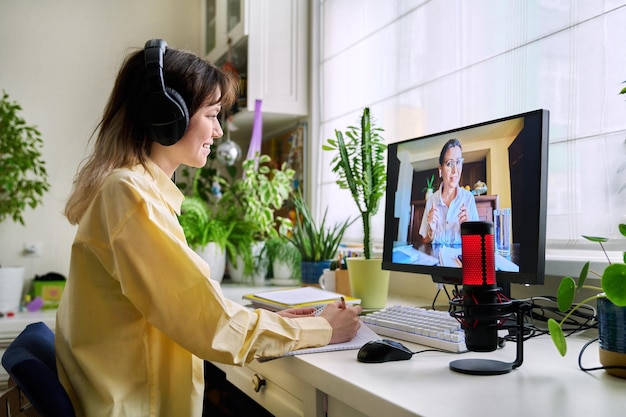 Teenage female student studying online at home female in headphones with notebook talking to teacher by video using computer Chat call conference elearning college high school technology concept