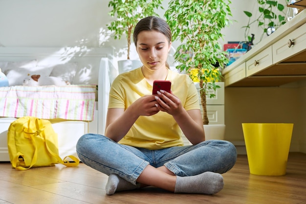 Teenage female using smartphone resting sitting at home on floor in room