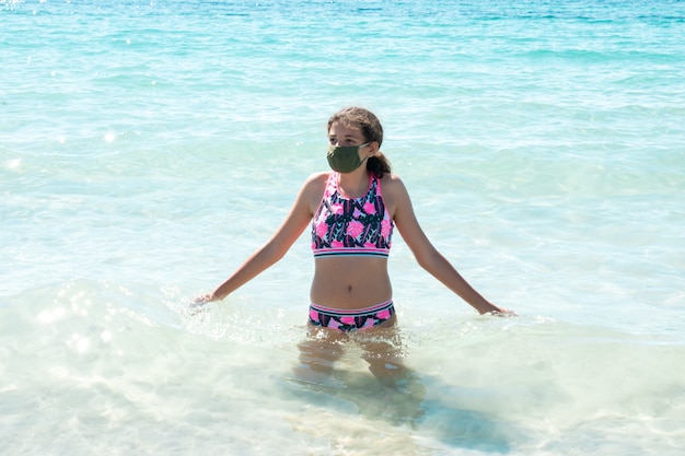 Teenage girl on the beach wearing a protective mask to prevent coronavirus disease