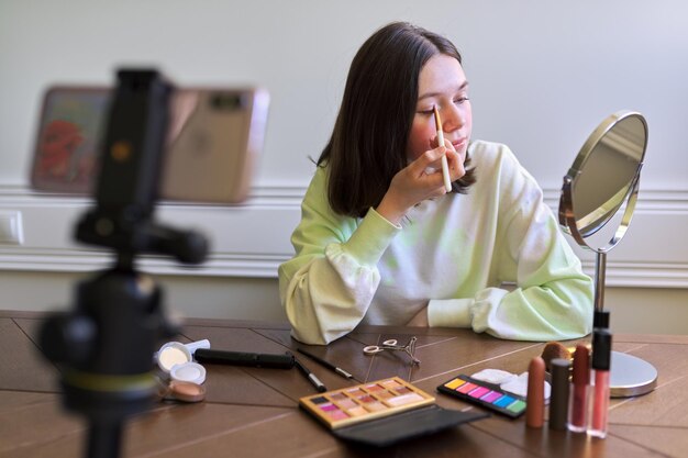 Photo teenage girl, beauty blogger filming video for channel blog, eyeshadow painting. telling and showing makeup and does invisible natural makeup. beauty, technology, communication teenagers online