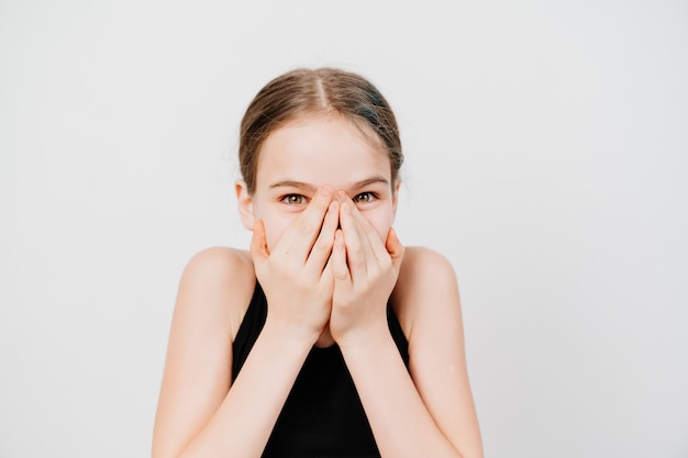 A teenage girl in a black T-shirt closes her mouth with her hands