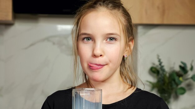 Teenage girl in black tshirt drinks fresh milk from glass\
licking white mustache on upper lip standing against marble wall in\
kitchen closeup