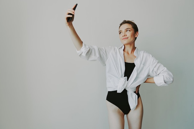 Teenage girl blogger takes photos and shoots herself on video on her phone for social media content video blogger selfies against a white wall with a smile at home freelancer