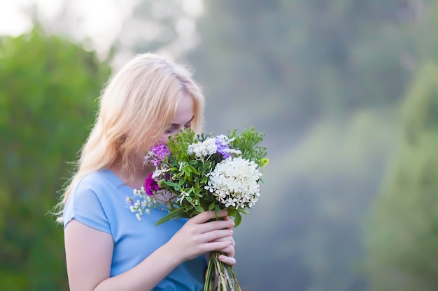 Photo a teenage girl in a blue dress walking on a foggy evening with a bouquet of beautiful garden flowers