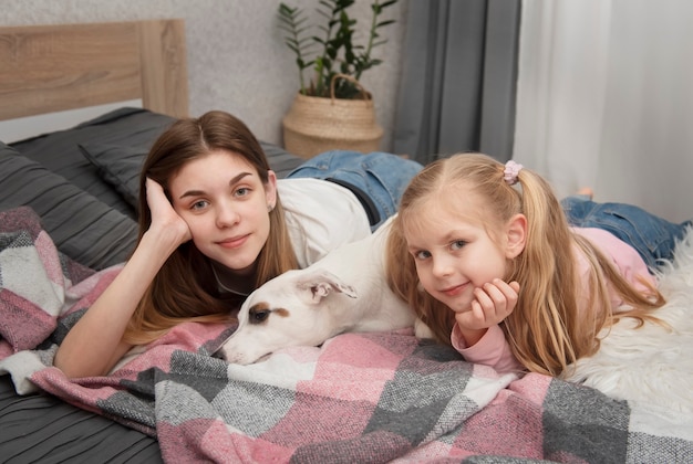 Teenage girl and child playing with their dog jack russell on the bed at home