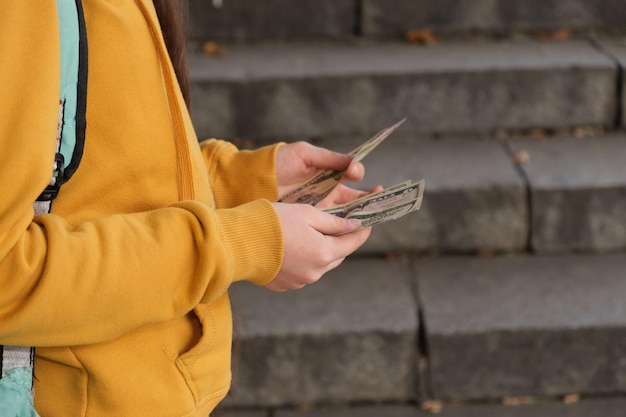 Teenage girl counts dollar bills on the background of the stairs