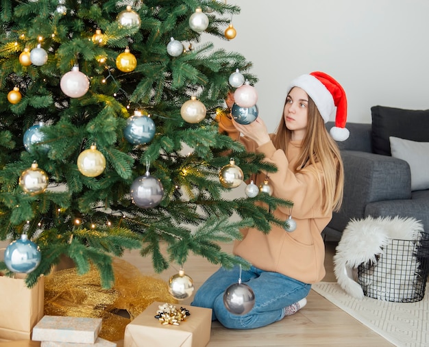 10대 소녀가 크리스마스 트리를 장식합니다. 거실에 있는 크리스마스 트리.
