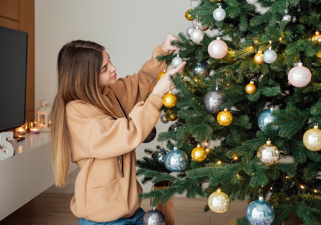 10代の少女がクリスマスツリーを飾ります。リビングルームのクリスマスツリー。