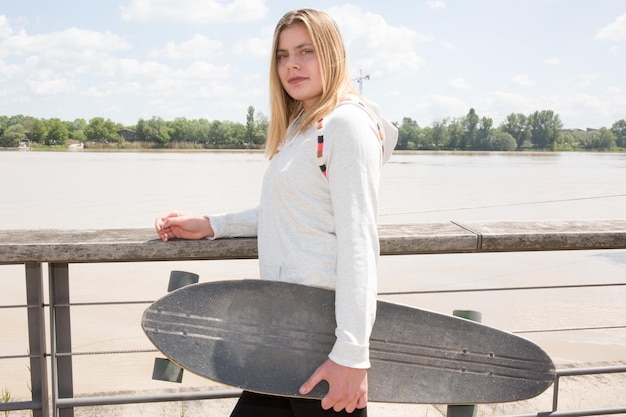 Teenage girl on the docks of the city with her skateboard under her arm