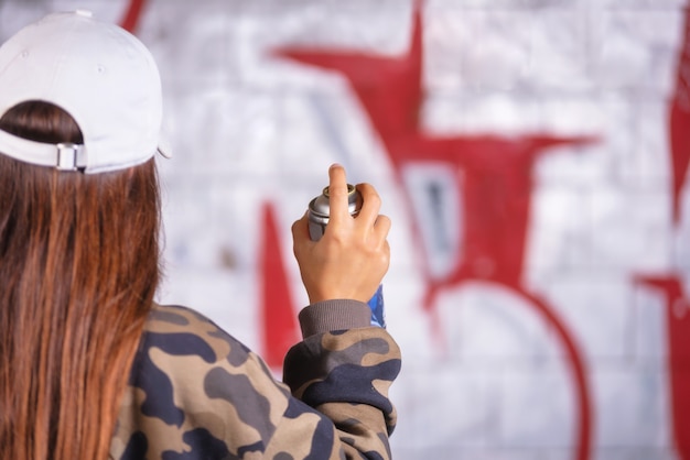 Teenage girl drawing graffiti with spray paint on street wall.