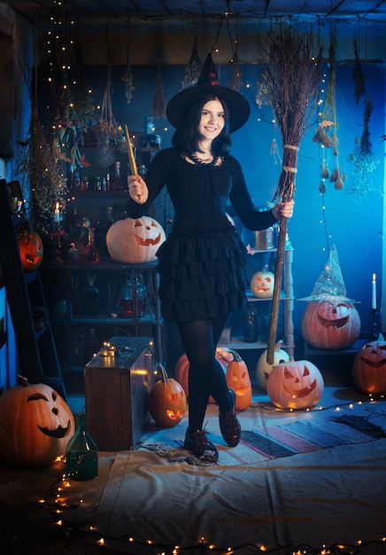 Teenage girl dressed as a witch with pumpkins on the background of decor for Halloween