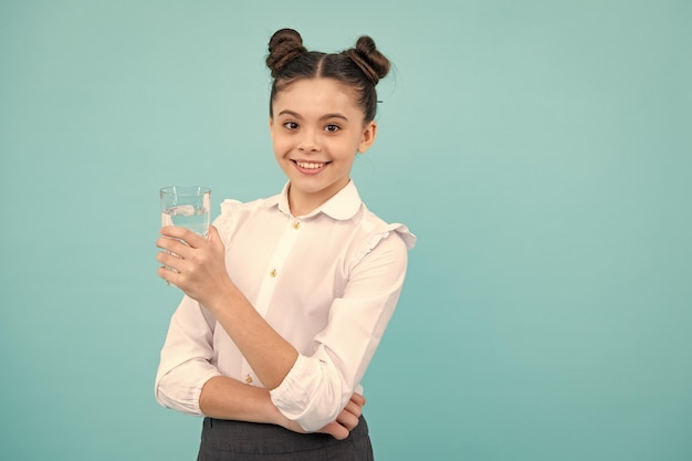 Девочка-подросток пьет воду из стекла на синем фоне Повседневная жизнь здоровье Пейте воду для здоровья и баланса тела Счастливый подросток позитивные и улыбающиеся эмоции девочки-подростка