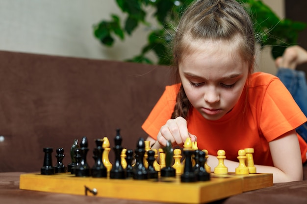 Una ragazza adolescente durante la quarantena gioca a scacchi a casa sdraiata sul divano