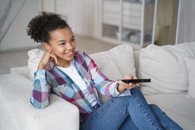 Teenage girl enjoying tv series watching and shifts channels Afro young woman has morning leisure