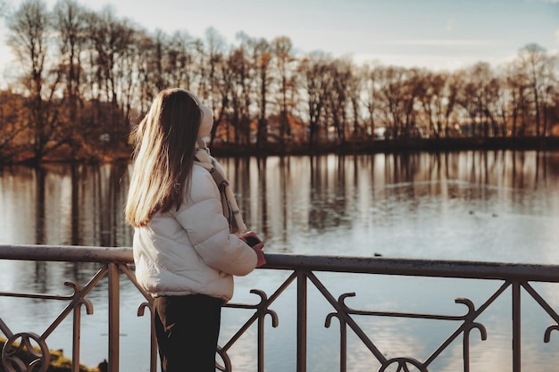 Adolescente da dietro che indossa abiti casual autunnali in un parco autunnale con lago all'aperto