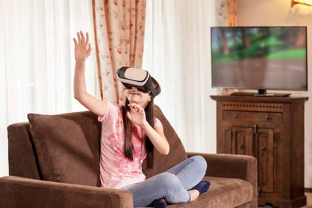 ティーンエイジャーの女の子が自宅のソファで仮想現実シミュレーターを使用している